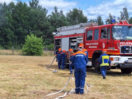 zeigt Feuerwehrmitglieder, die am Feuerwehrauto Schläuche aufrollen