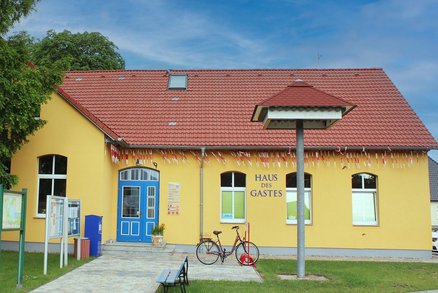 zeigt Blick auf das Haus des Gastes mit gelber Fassade und rotem Ziegeldach, davor ein Schwalbenhaus