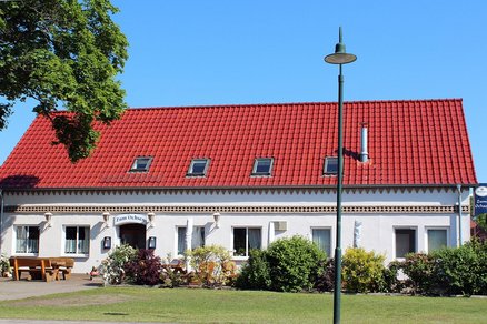 zeigt Gebäude mit weißem Putz, rotem Ziegeldach und der Beschriftung "Zum Ochsen", davor eine Strauchhecke und eine hölzerne Sitzgruppe
