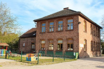 zeigt 2-geschossiges Klinkergebäude mit eingezäuntem Kinderspielpatz
