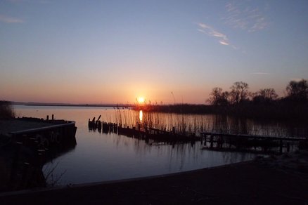 zeigt Sonnenuntergang über dem Haff, mit Holzbootsstegen und Schilfgürtel im Vordergrund
