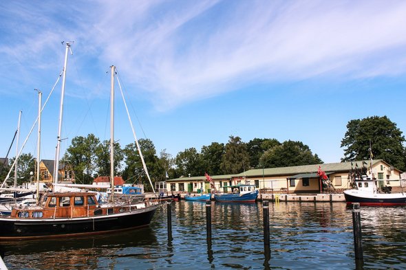 Der Hafen in Altwarp/Dorf mit dem angrenzenden Badestrand ist einen Abstecher wert. Gleich daneben in der Tourismusinformation gibt man gern interessante Ausflugstipps. zeigt Blick in den Hafen mit Booten und Gebäuden