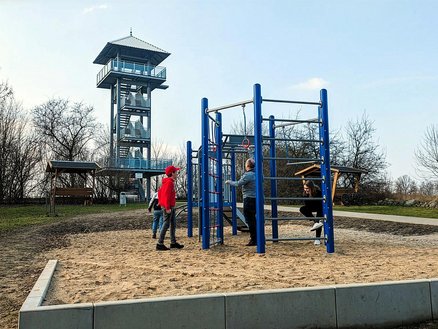 zeigt Aussichtsturm auf dem Apothekerberg und an einem Klettergerät spielende Kinder