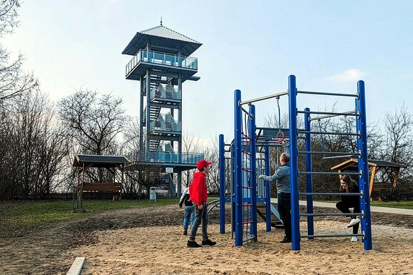Vom Aussichtsturm auf dem Apothekerberg hat man einen grandiosen Rundumblick. Picknickgarnituren und Spielgerät für die Jüngsten laden zu kurzweiligem Zeitvertreib ein. zeigt Aussichtsturm auf dem Apothekerberg und Spielgerüst mit spielenden Kindern