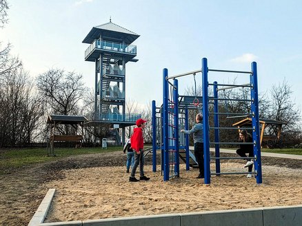 zeigt Aussichtsturm auf dem Apothekerberg und an einem Klettergerät spielende Kinder