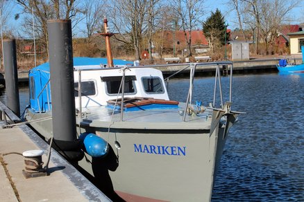 zeigt ein am Hafenbecken grau-weißes Boot mit der Aufschrift "Mariken"