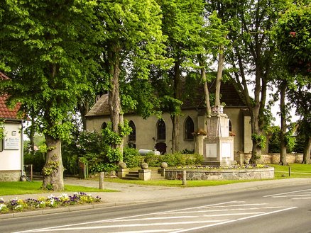 zeigt Kirchengebäude und Mahnmal zum Gedenken der Kriegsgefallenen