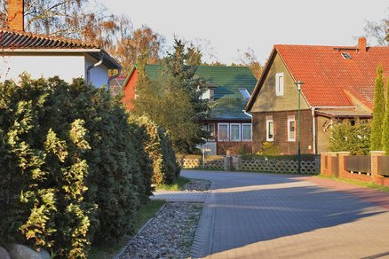 zeigt eine gepflasterte Straße mit angrenzenden Holzhäusern und ihre Vorgärten