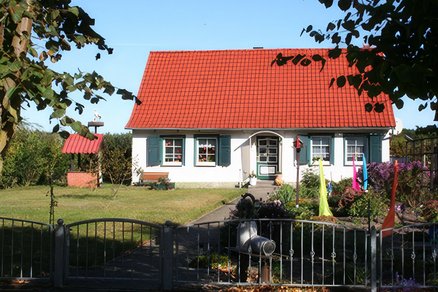 zeigt Wohngrundstück mit Haupthaus, bunt dekoriertem Garten davor und schmiedeeisernem Zaun