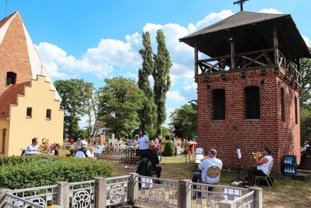 zeigt musizierende Menschen auf dem Friedhof mit Kirche und Glockentum