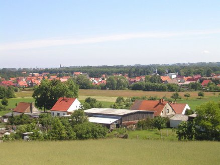 zeigt Blick über die Ortslage hinweg mit verschiedenen Gebäuden, Wiesen- und Ackerflächen