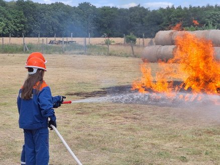 zeigt Mitglied der Jugendfeuerwehr, das mit einem Wasserschlauch ein Feuer löscht