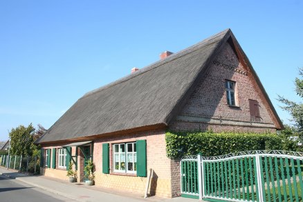 zeigt gelbliches Klinkerwohnhaus mit Schilfdach an einer Straße