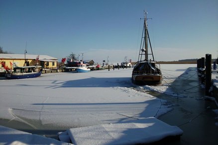zeigt Winteransicht des eingefrorenen und beschneiten Hafenbeckens mit Schiffen