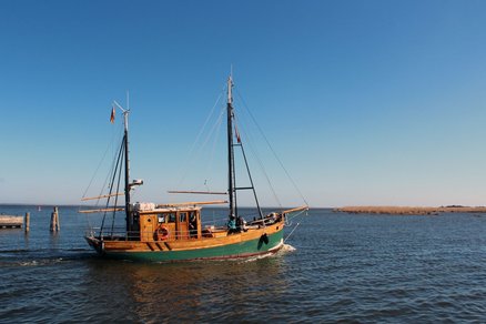zeigt einen grünen Holzsegelkutter auf dem Wasser
